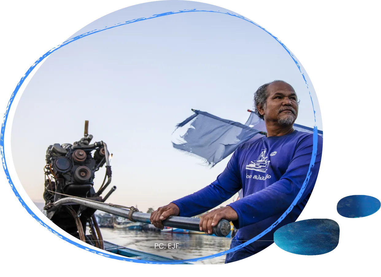 A small-scale fisher steering his boat at sea, a blue sail catching the wind behind him.