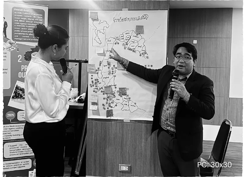 A speaker addressing a workshop beside a large hand-drawn map of Thailand’s coastal provinces.