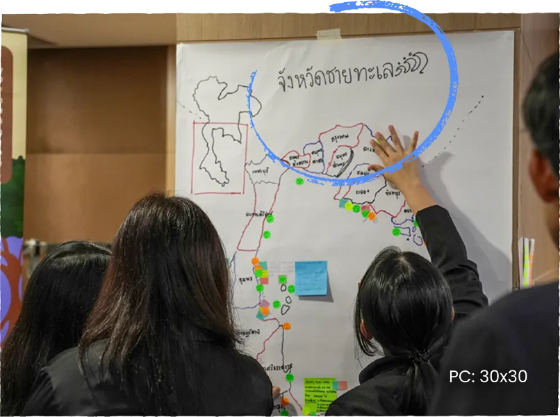 Workshop participants gathered around a hand-drawn map of Thailand’s coastal provinces, marking it with coloured dots.