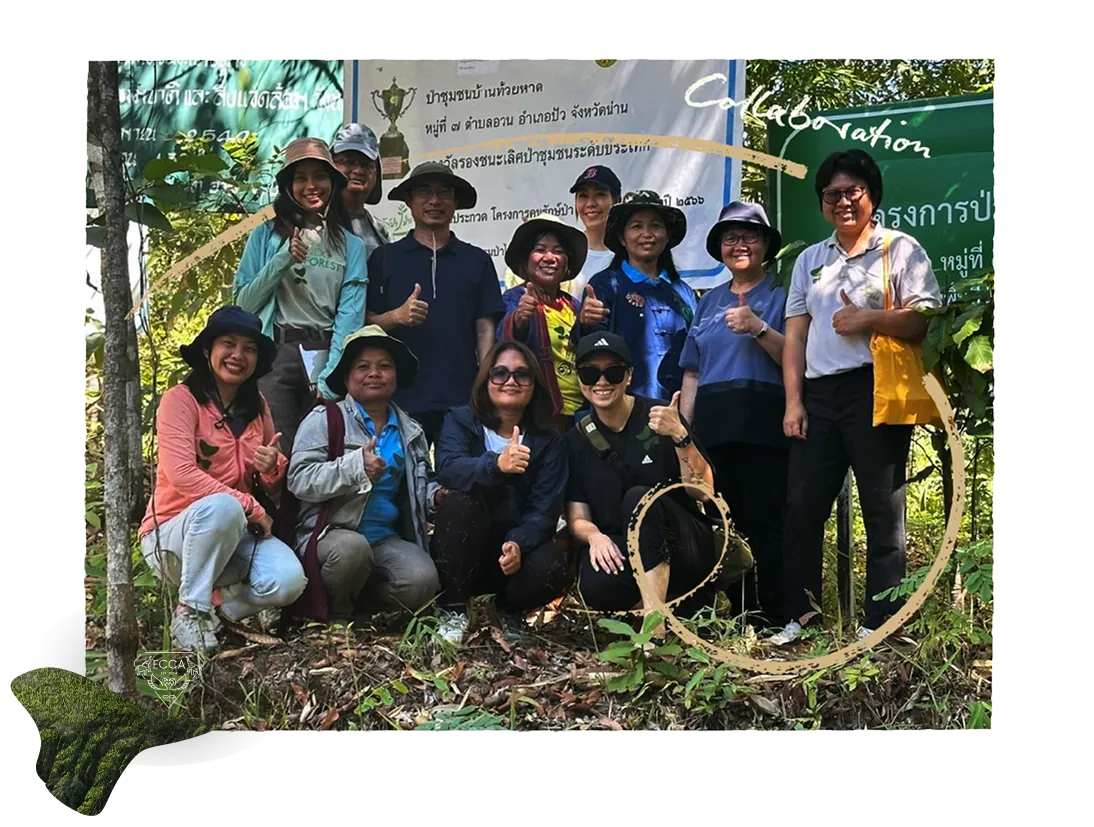 Community forestry participants posing together in the forest beneath a Thai-language banner.