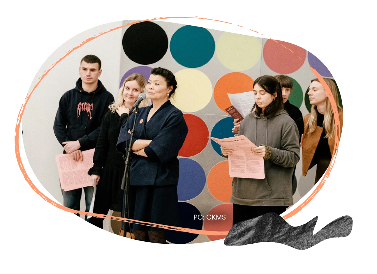 Participants holding printed sheets, standing in front of a wall of coloured circles.